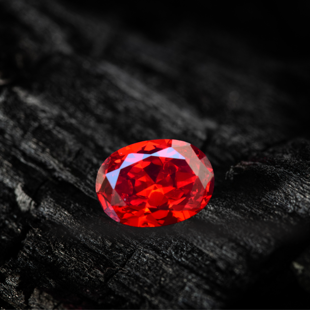 Rubis naturel rouge taillé en ovale, posé sur une surface sombre. Pierre précieuse éclatante aux reflets profonds et intenses.