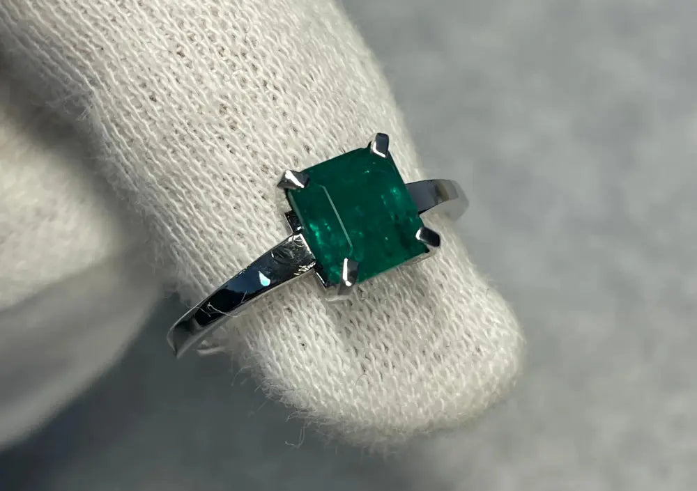 Bague sur-mesure en or blanc sertie d’une émeraude verte taille carrée, créée pour une cliente en quête d’élégance intemporelle.