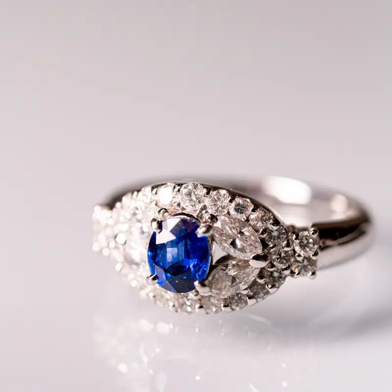 Superbe bague sur-mesure ornée d'un saphir bleu taille ovale, serti dans une monture en or blanc incrustée de diamants scintillants. Un bijou raffiné et élégant, idéal pour une demande en mariage ou un cadeau d'exception. Conception réalisée avec des pierres précieuses authentiques et un savoir-faire artisanal unique. Mael Gems conçoit des bijoux sur mesure pour ses clients. La base est bien sûr une pierre précieuse d'exception.