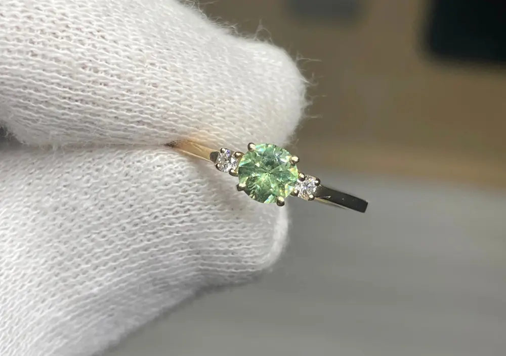 Bague fine en or jaune sertie d’une tourmaline verte centrale, accompagnée de petits diamants, conçue pour un bijou raffiné et lumineux.