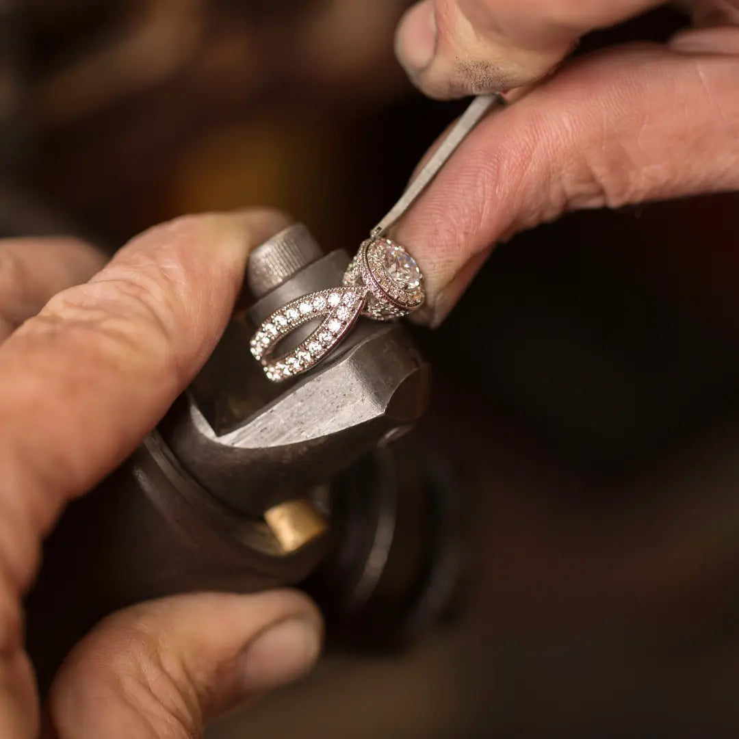 Main d’un artisan sertissant une bague en or ornée de diamants dans un atelier de joaillerie, illustrant la création de bijoux sur mesure.
Sertissage d’une bague sur mesure dans un atelier de joaillier artisan.
