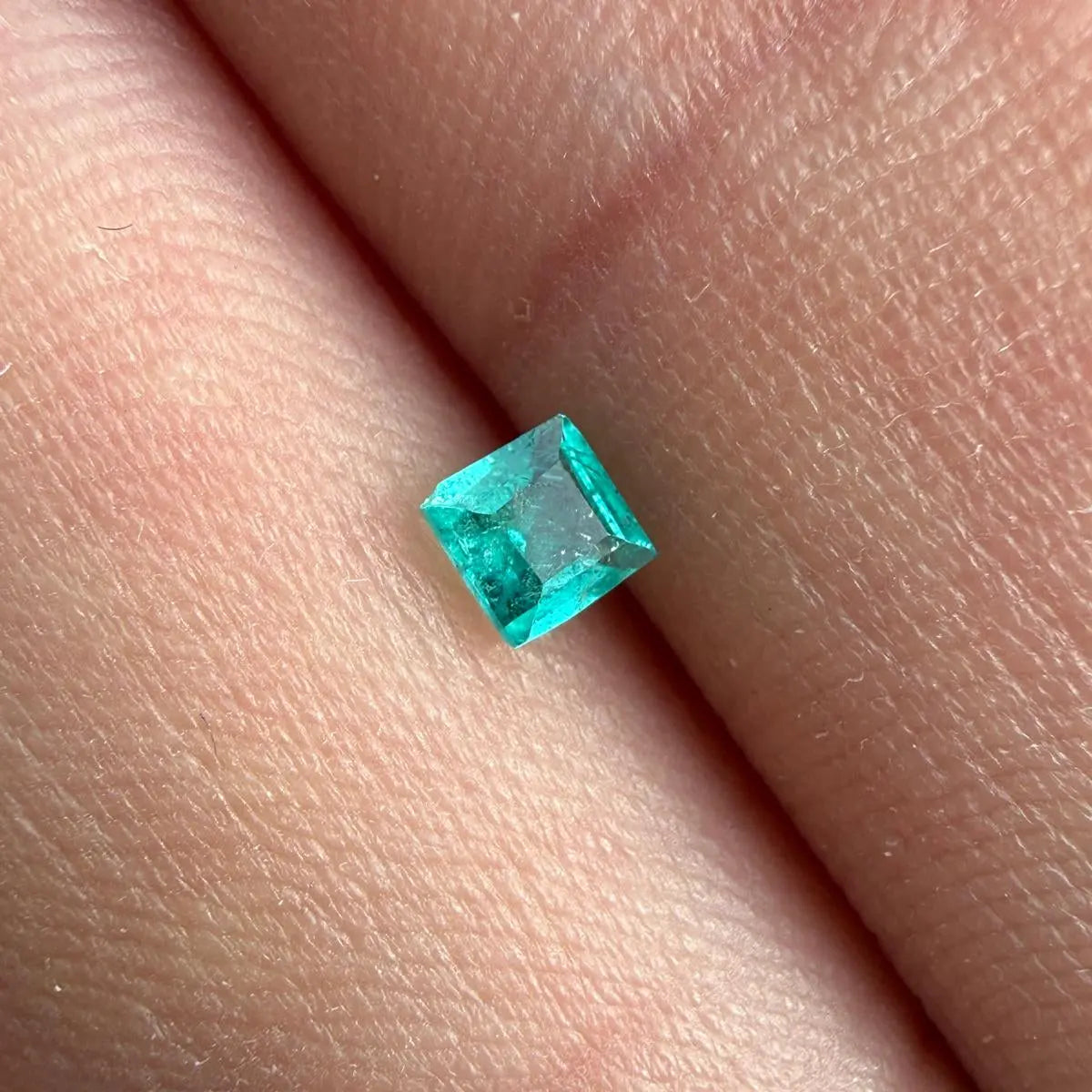 Une petite pierre précieuse de forme carrée, d'un bleu néon. Cette pierre précieuse présente un aspect brillant et étincelant.