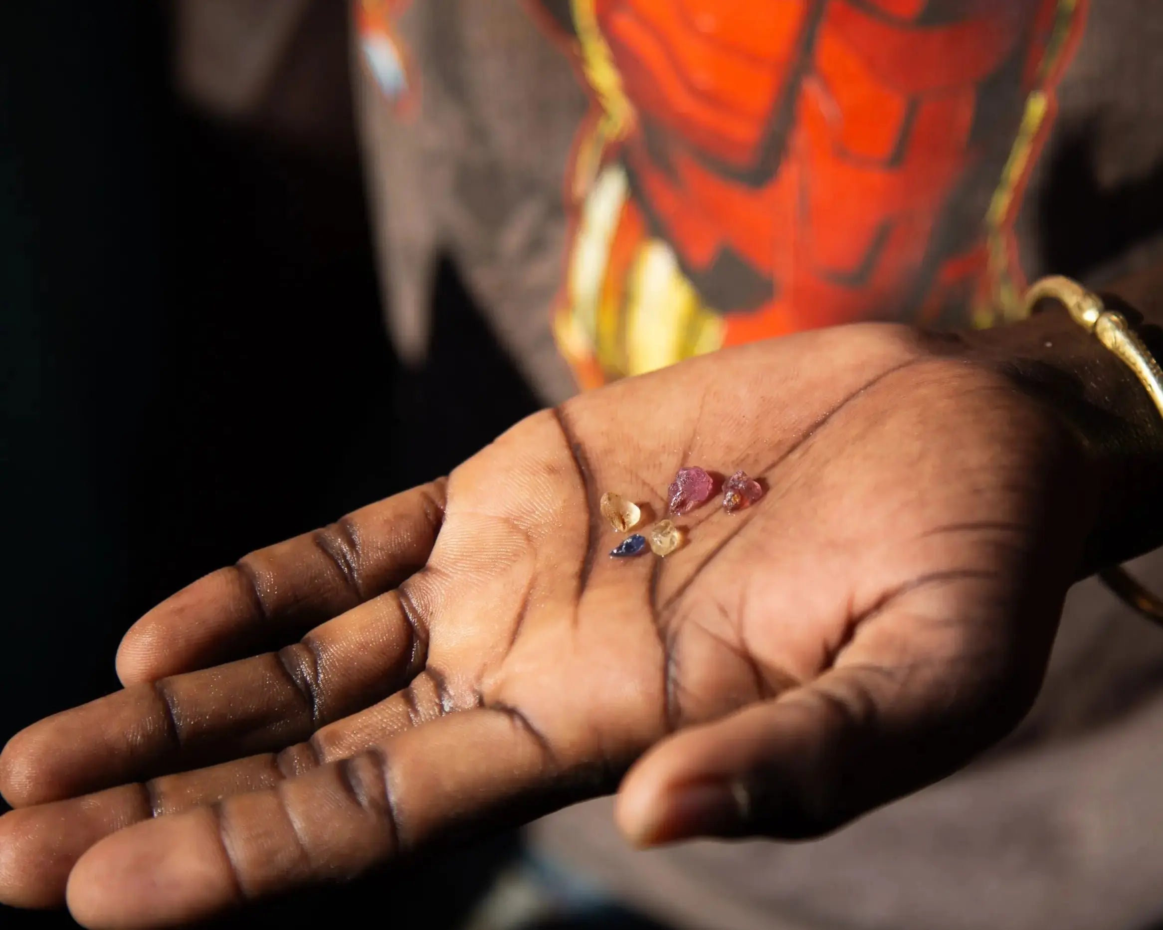 Main d’un artisan tenant plusieurs pierres précieuses brutes multicolores, issues d’une extraction artisanale.

Pierres précieuses brutes dans la main d’un artisan, prêtes à être taillées.

